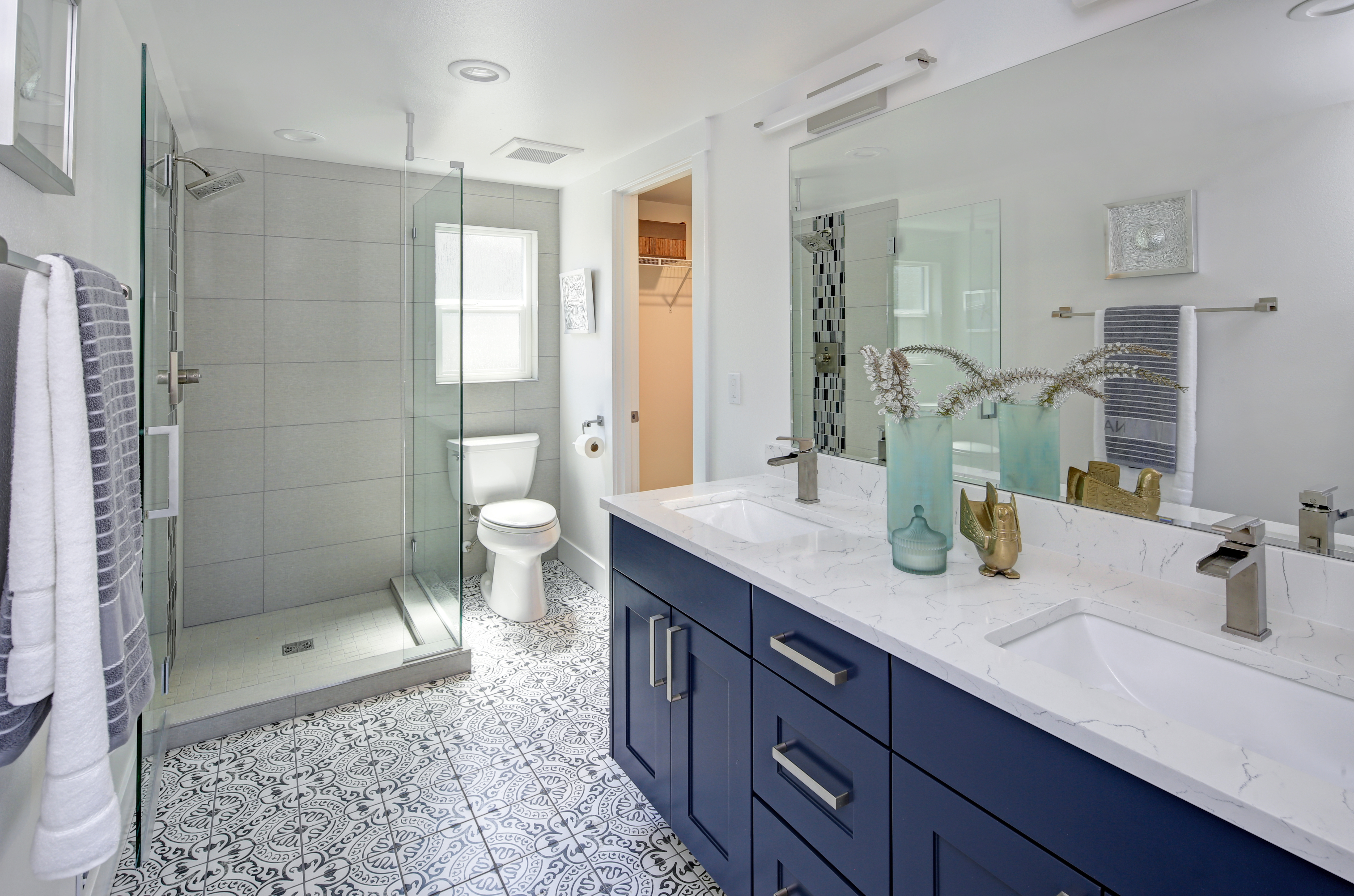 Modern bathroom with navy vanity, marble countertop, glass shower enclosure, and patterned tile flooring