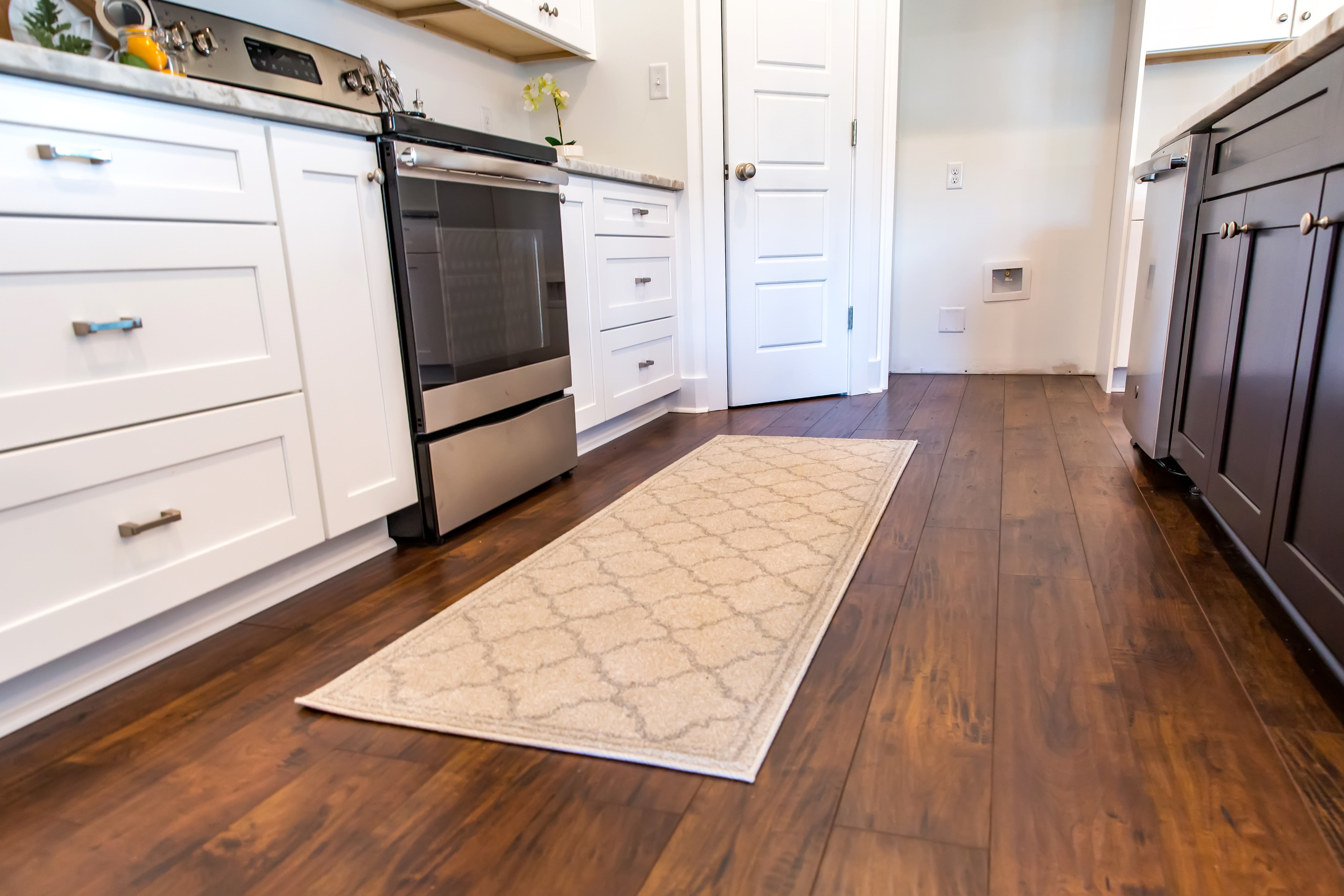 Modern kitchen with white cabinetry, stainless steel oven, dark wood flooring and beige runner rug