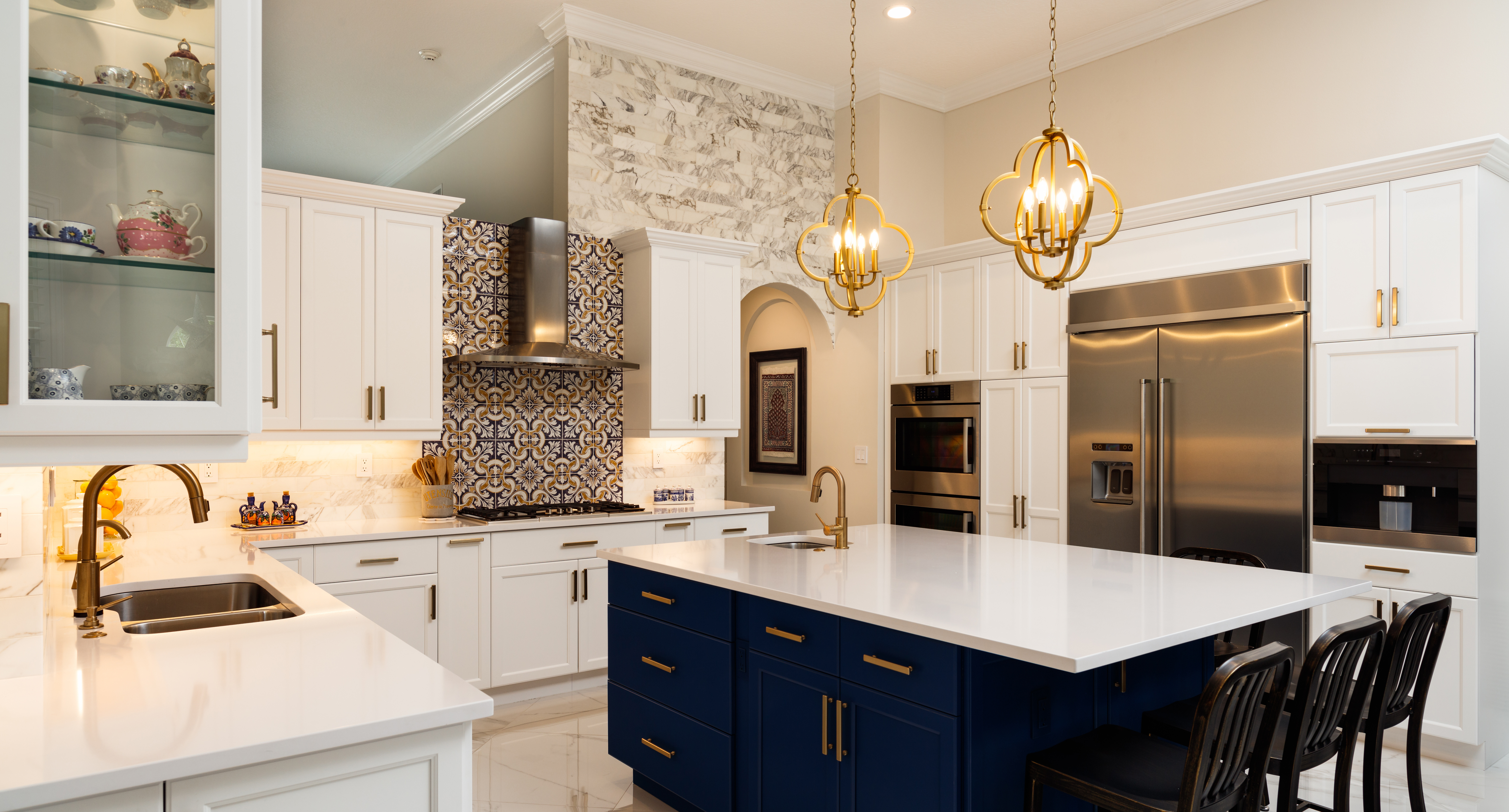 Luxury kitchen with white cabinetry, navy island, marble backsplash, gold fixtures and pendant lights