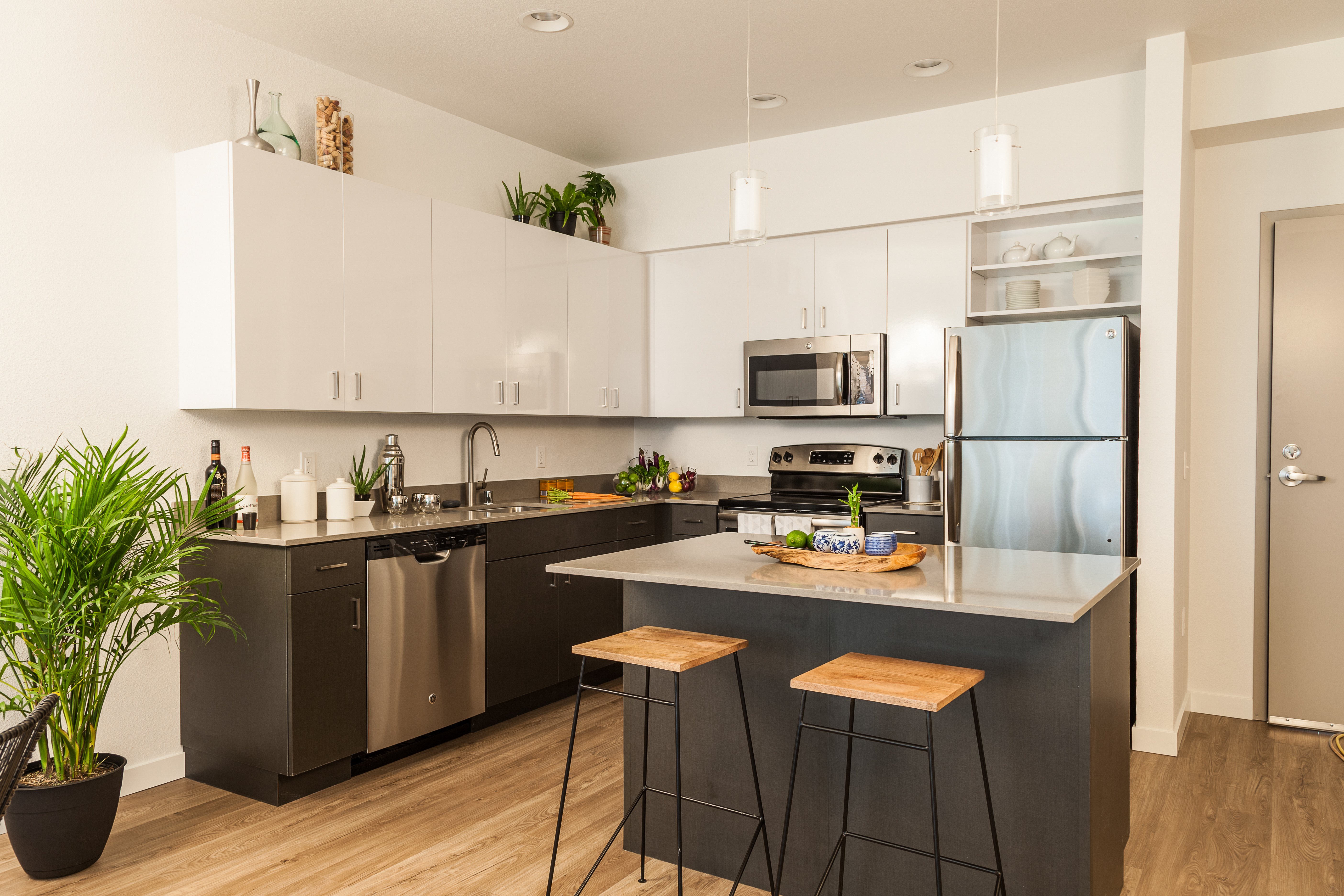 Modern kitchen with white upper cabinets, dark lower cabinets, stainless steel appliances, and island with wooden bar stools